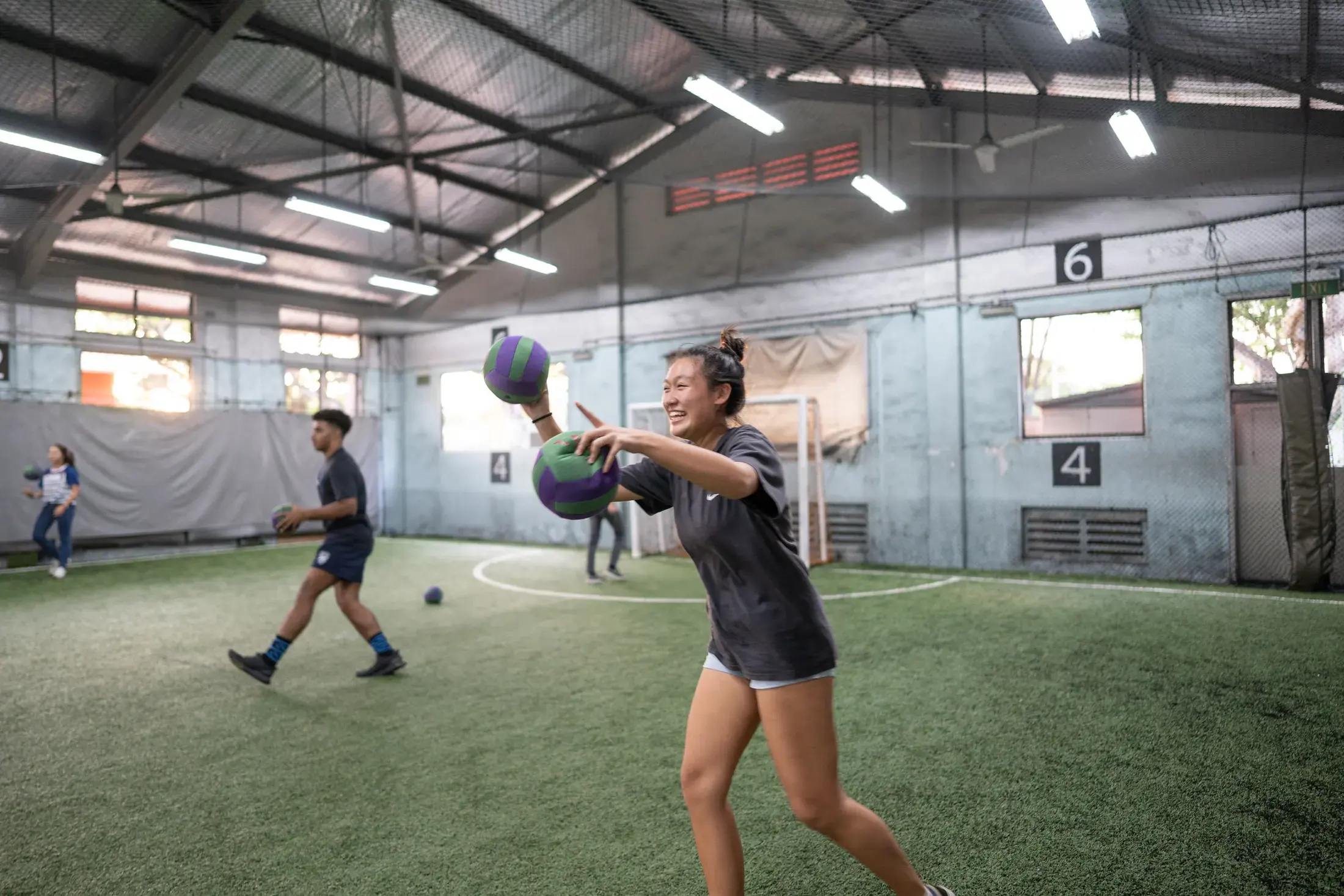 A smiling Dodgeball player holding two soft balls on an indoor court